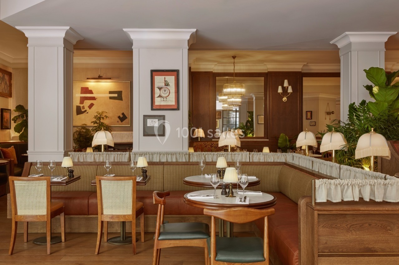 Salle de restaurant élégante avec banquettes en bois, tables dressées et éclairage chaleureux.