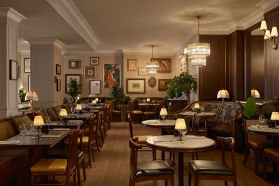 Chambre lumineuse avec lit double, fauteuil jaune, commode en bois et grande fenêtre donnant sur des immeubles parisiens.