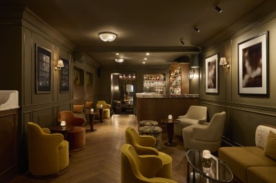 Chambre lumineuse avec lit double, fauteuil jaune, commode en bois et grande fenêtre donnant sur des immeubles parisiens.