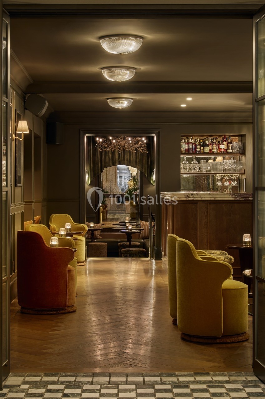 Intérieur d'un bar élégant avec fauteuils colorés, éclairage tamisé et comptoir en bois.