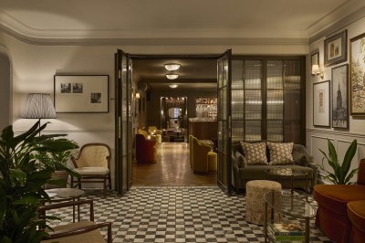 Chambre lumineuse avec lit double, fauteuil jaune, commode en bois et grande fenêtre donnant sur des immeubles parisiens.