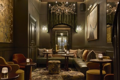 Chambre lumineuse avec lit double, fauteuil jaune, commode en bois et grande fenêtre donnant sur des immeubles parisiens.