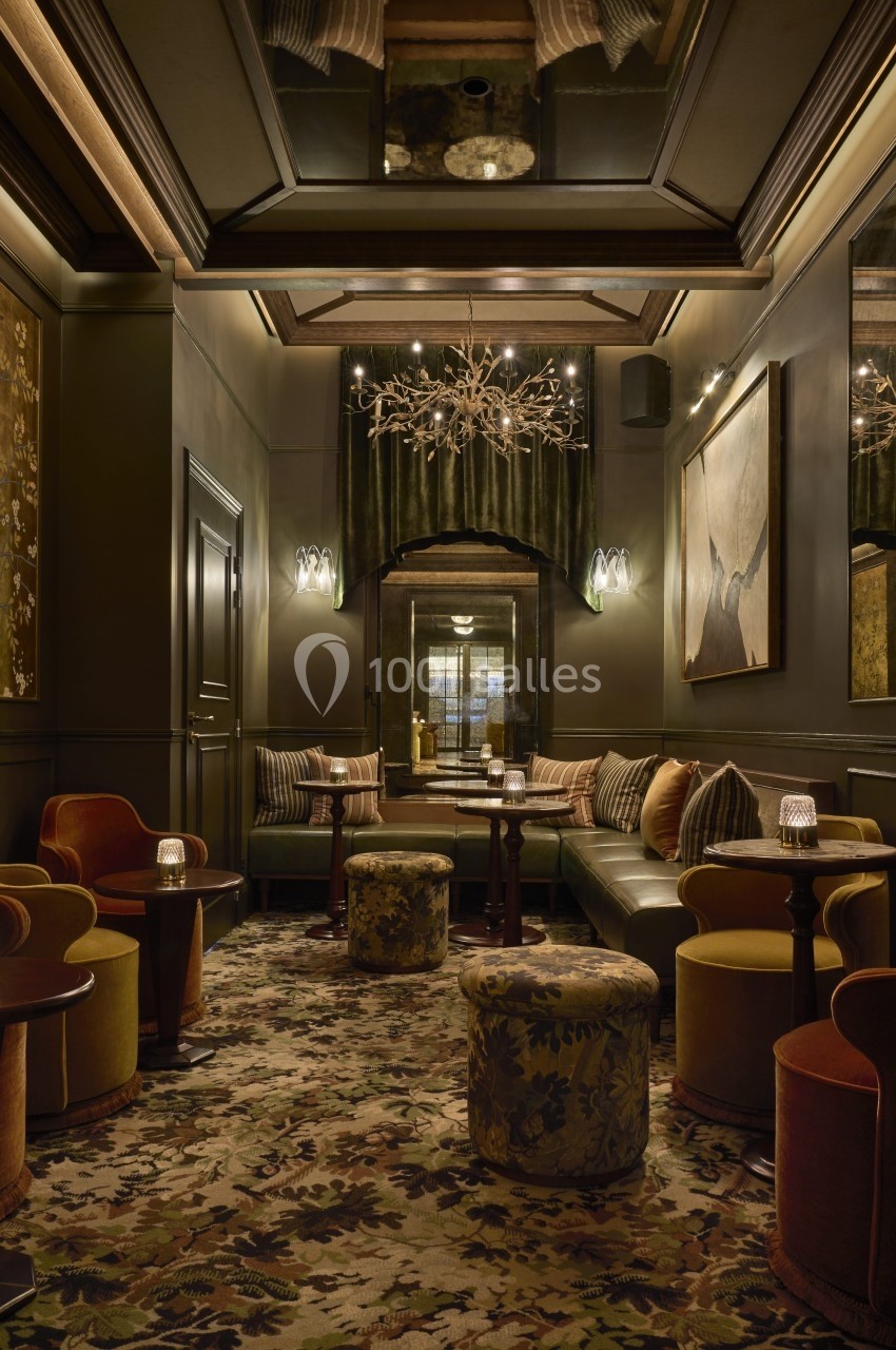 Salon élégant avec fauteuils colorés, tables basses, lustre décoratif et tapis à motifs dans une ambiance tamisée.