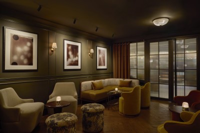 Chambre lumineuse avec lit double, fauteuil jaune, commode en bois et grande fenêtre donnant sur des immeubles parisiens.