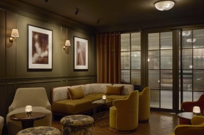 Chambre lumineuse avec lit double, fauteuil jaune, commode en bois et grande fenêtre donnant sur des immeubles parisiens.