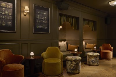 Chambre lumineuse avec lit double, fauteuil jaune, commode en bois et grande fenêtre donnant sur des immeubles parisiens.