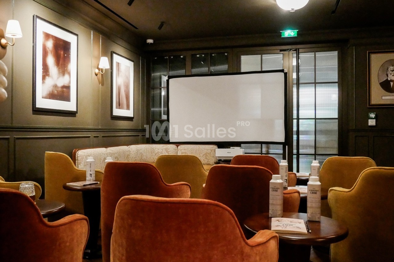 Salle de réunion avec fauteuils colorés, écran de projection, tables basses et décorations murales.