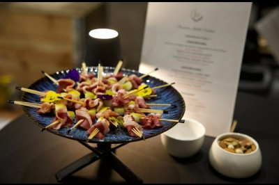 Buffet avec amuse-bouches variés, boissons en carafes et seau à glace sur une table blanche en extérieur.