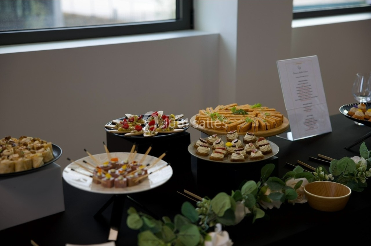 Plateau de buffet avec divers amuse-bouches disposés sur des présentoirs noirs, décorés de verdure.
