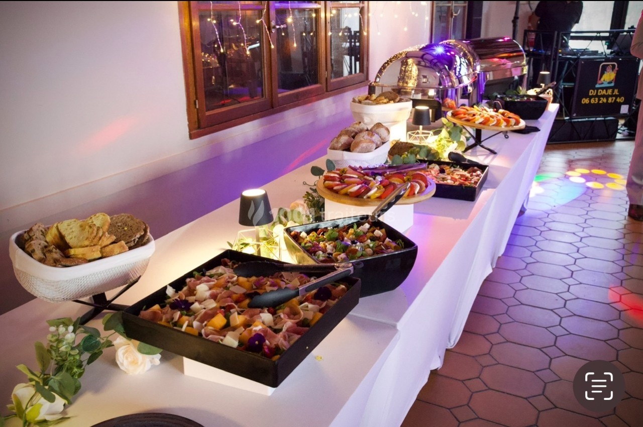 Buffet avec plats variés, salades, pains et plateaux de charcuterie, disposés sur une table blanche éclairée.