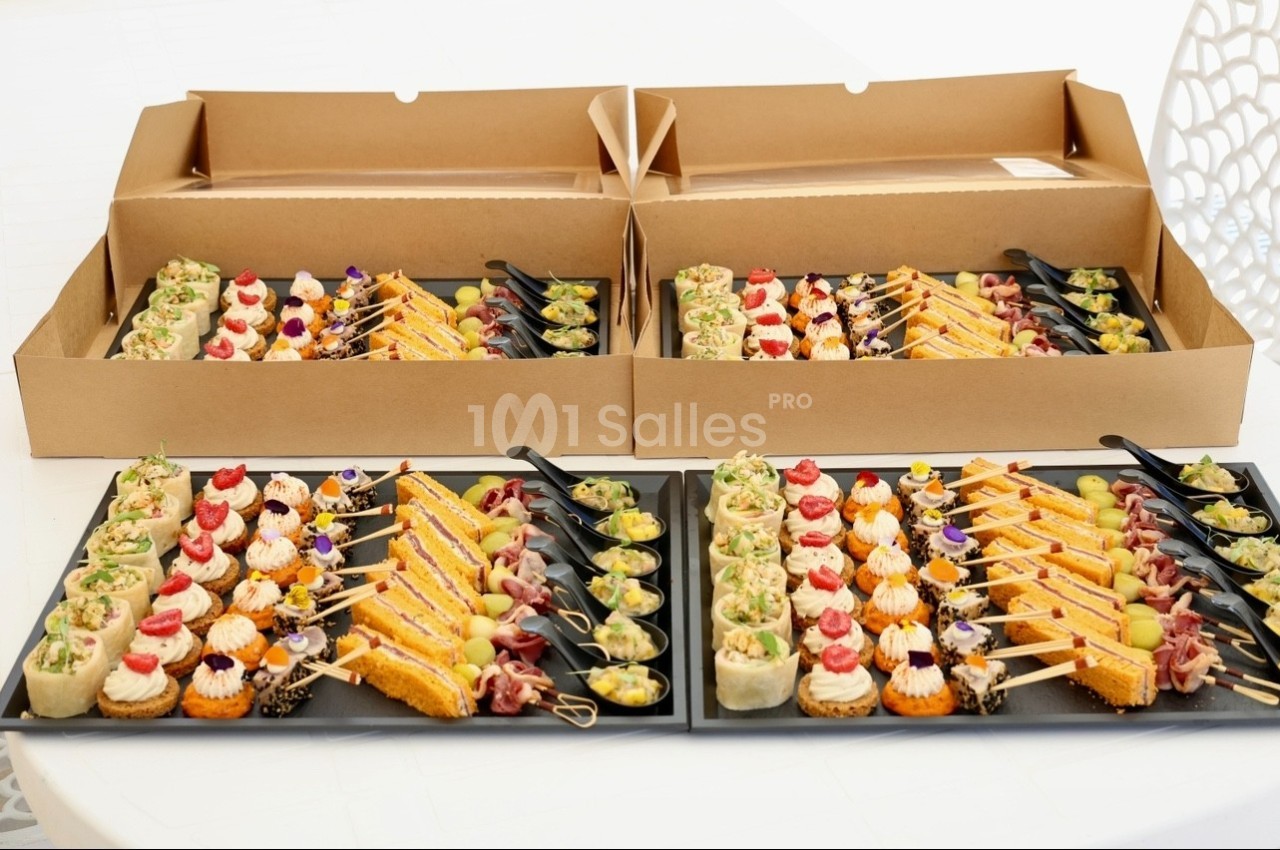 Plateaux de bouchées apéritives variées disposées sur des plateaux noirs et présentées dans des boîtes en carton.