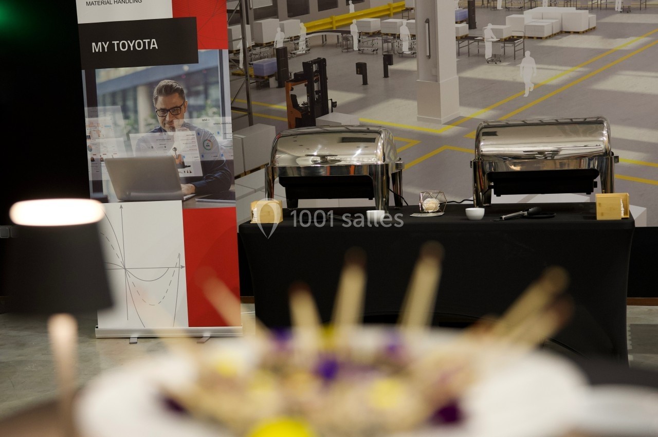 Buffet avec plats chauds en arrière-plan, accompagné d'une bannière promotionnelle Toyota dans un espace industriel.