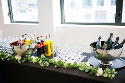 Buffet avec verrines, amuse-bouches, boissons en carafes et seau à glace sur une nappe blanche.