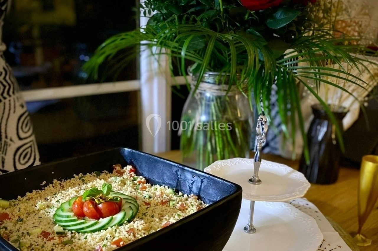 Plat de taboulé garni de concombres et tomates cerises, posé sur une table décorée avec des fleurs et des assiettes.