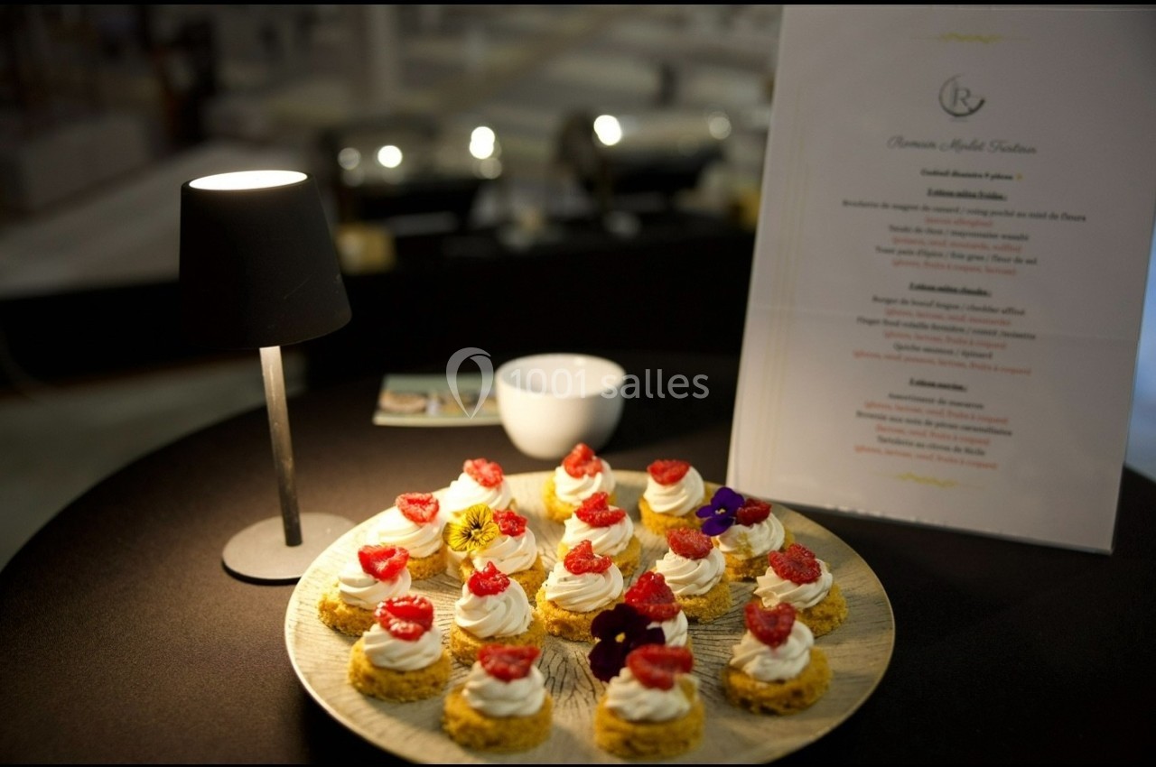 Assortiment de desserts individuels décorés de framboises et fleurs comestibles, présenté sur une table sombre.