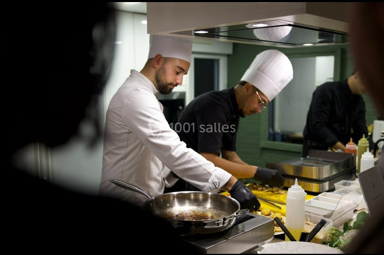 Deux chefs cuisiniers en tenue blanche préparent des plats dans une cuisine professionnelle.