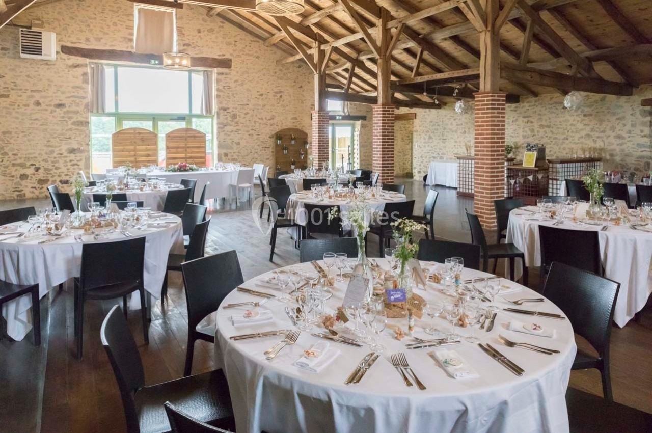 Salle de réception avec tables rondes dressées, nappes blanches, chaises noires et décoration florale.