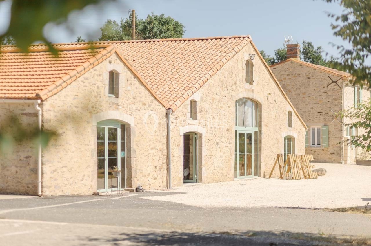 Bâtiment en pierre avec toit en tuiles rouges, grandes baies vitrées et espace extérieur ensoleillé.