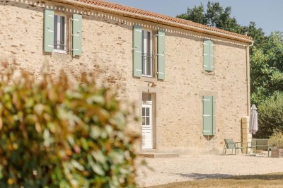 Salle à manger avec une grande table entourée de chaises, cuisine équipée à gauche et salon avec canapé au fond.