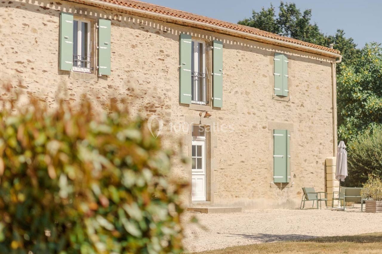 Façade en pierre d'une maison avec volets verts, entourée de végétation et d'un espace extérieur aménagé.