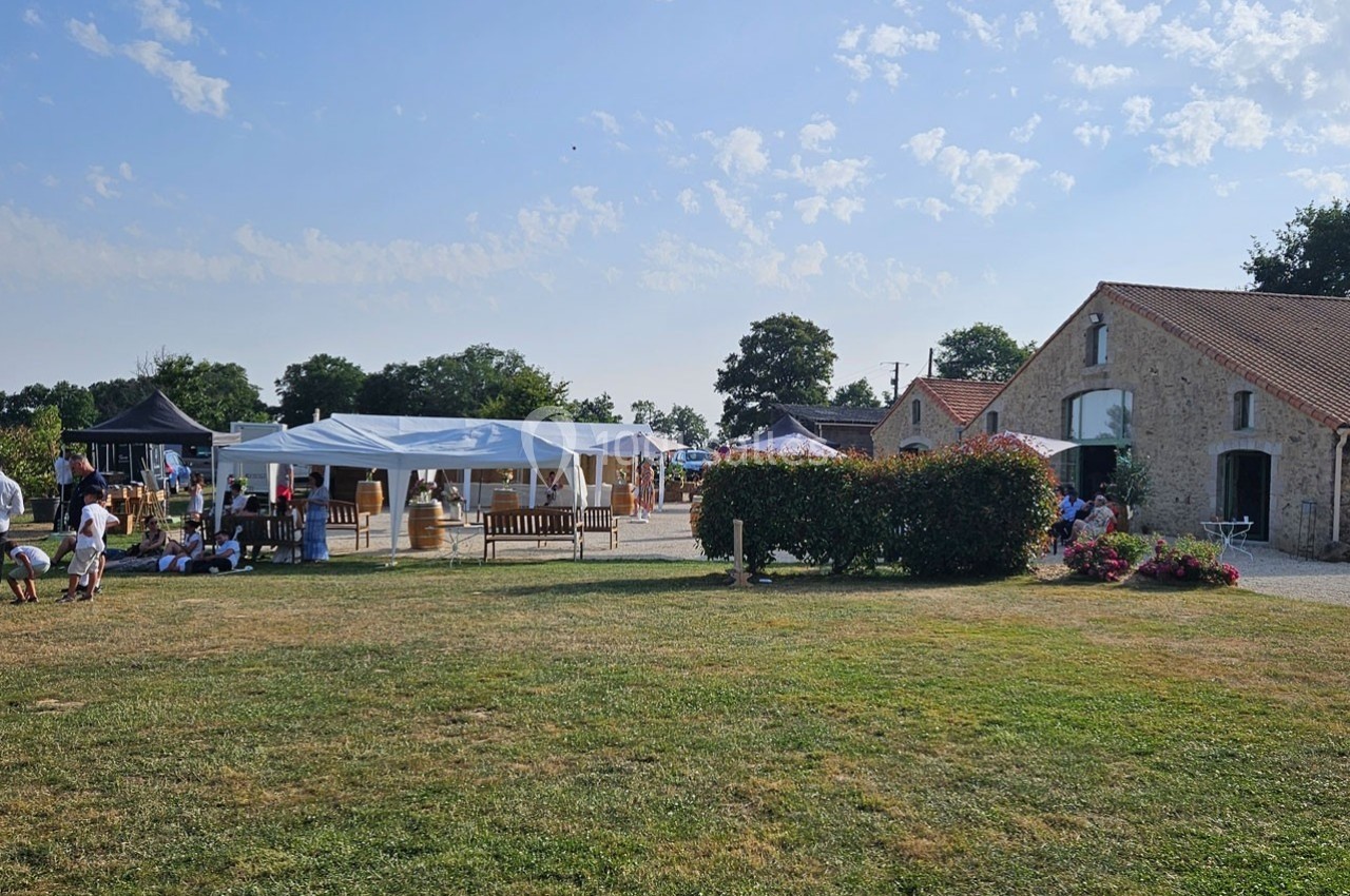 Un espace extérieur avec pelouse, barnum, tables et une bâtisse en pierre, lors d'un événement en plein air.