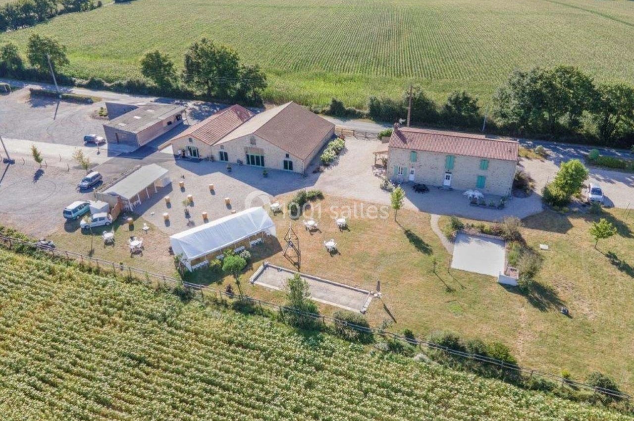 Vue aérienne d'un domaine rural avec bâtiments, chapiteau, espaces verts et champs environnants.