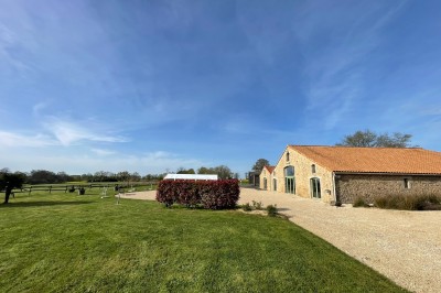 Salle à manger avec une grande table entourée de chaises, cuisine équipée à gauche et salon avec canapé au fond.