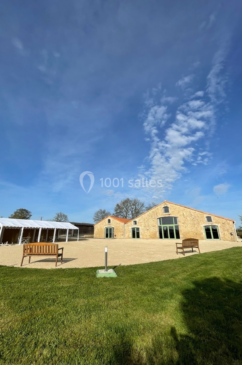 Bâtiment en pierre avec grandes fenêtres, entouré d'une pelouse et d'un ciel dégagé.
