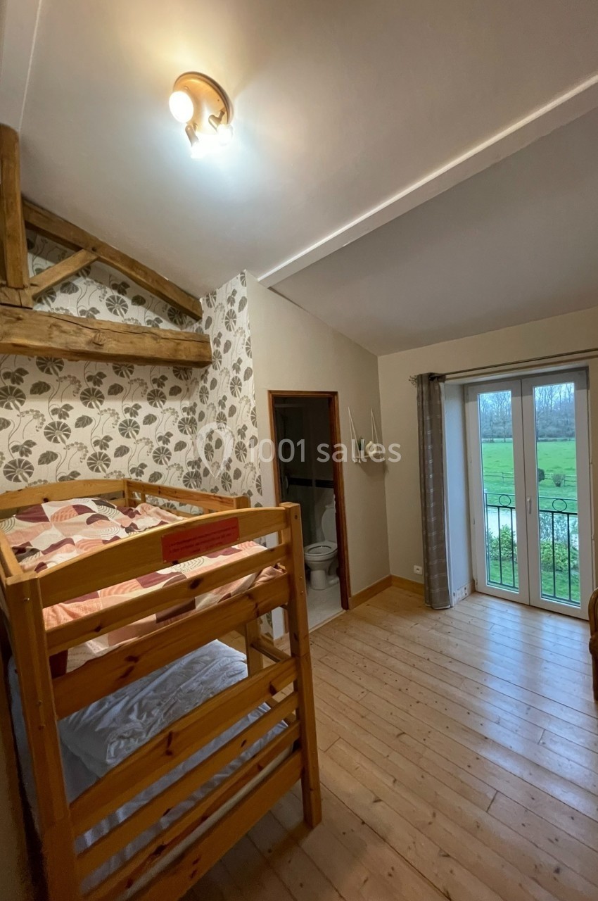 Chambre avec lits superposés en bois, parquet, papier peint floral, porte-fenêtre donnant sur un jardin.