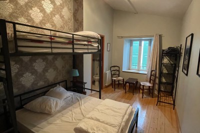 Chambre avec lit superposé, lit double, parquet en bois, fenêtre lumineuse et mobilier simple.