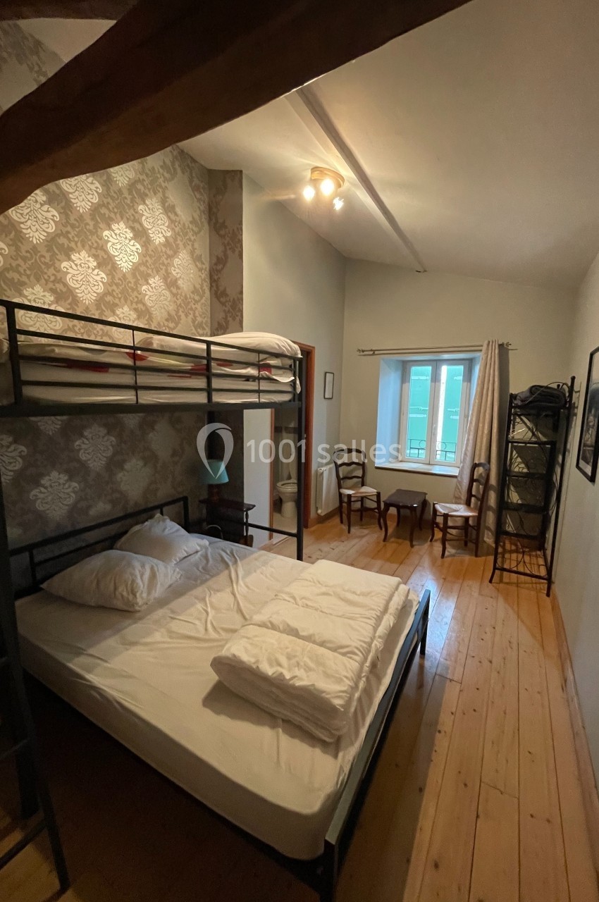 Chambre avec lit superposé, lit double, parquet en bois, fenêtre lumineuse et mobilier simple.