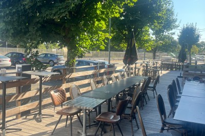 Miniature Location salle Canéjan (Gironde) - Forever Padel #4 Terrasse en bois avec tables et chaises disposées sous des arbres, bordée par une route et des voitures stationnées.