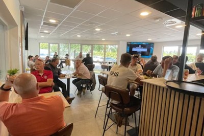 Miniature Location salle Canéjan (Gironde) - Forever Padel #6 Terrasse en bois avec tables et chaises disposées sous des arbres, bordée par une route et des voitures stationnées.