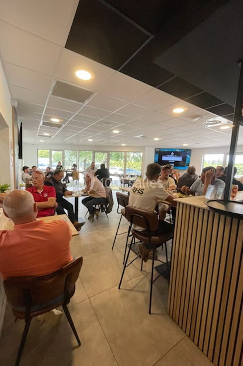 Des personnes assises dans un café lumineux, discutant autour de tables et du comptoir, avec vue sur l'extérieur.
