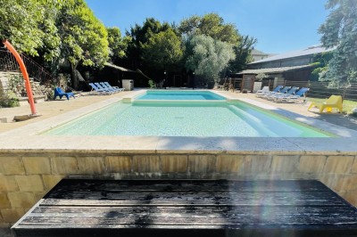 Piscine extérieure avec bassin principal et pataugeoire, entourée de chaises longues et d'arbres.