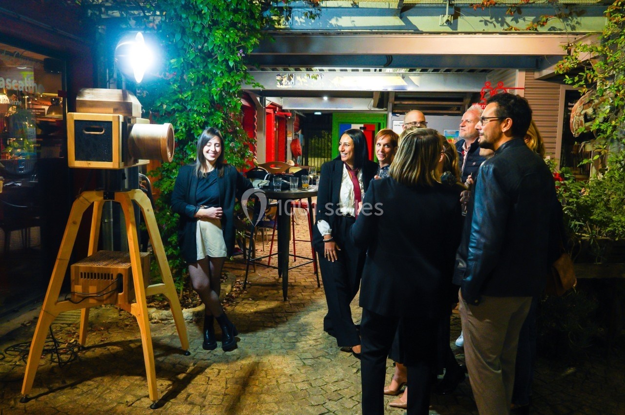 Un groupe de personnes debout en extérieur, rassemblé autour d'un appareil photo vintage sur trépied.