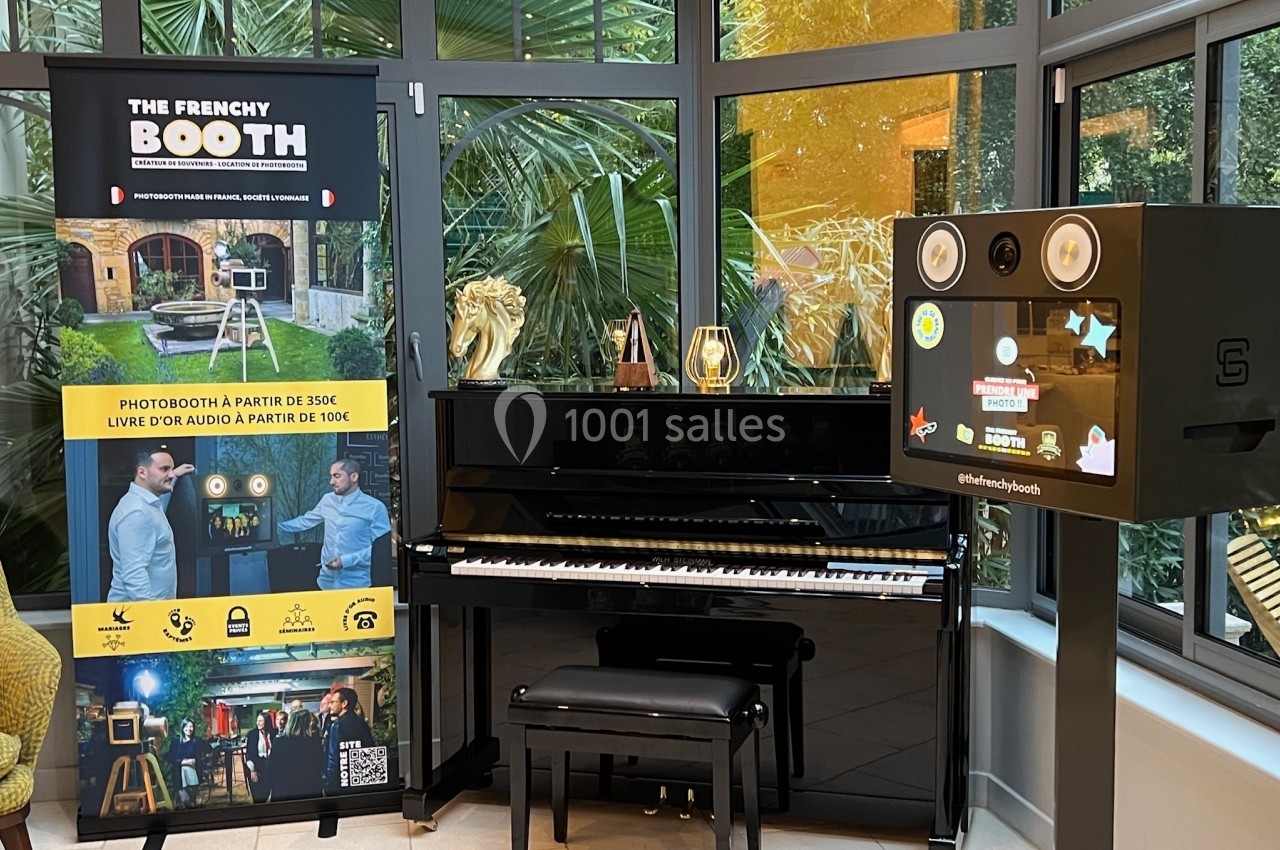 Piano noir devant une baie vitrée, accompagné d'une borne photo et d'un panneau promotionnel.