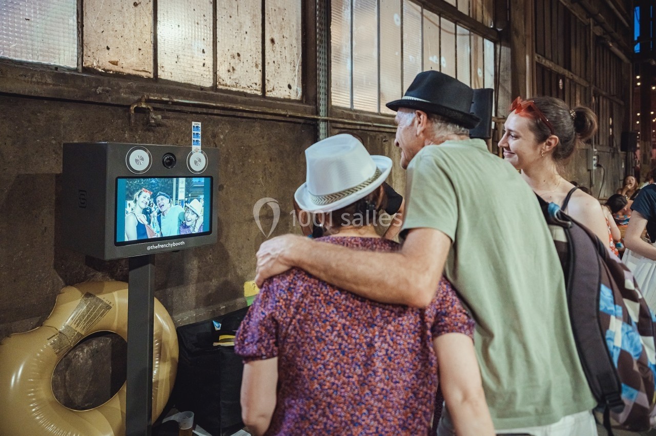 Trois personnes regardent un écran affichant leur photo prise dans un photobooth, dans un lieu industriel.