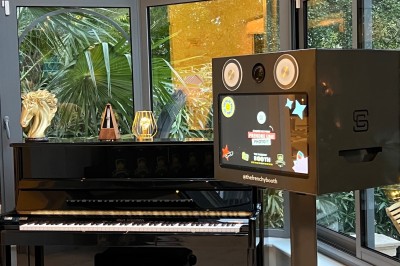 Une borne photo en bois avec écran et accessoires, entourée de personnes discutant dans un espace industriel.