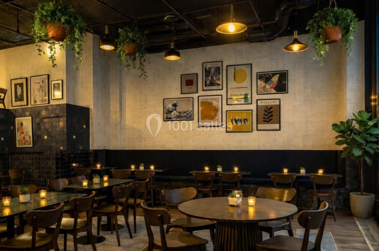 Salle de restaurant chaleureuse avec des tables en bois, des bougies allumées et des plantes suspendues.