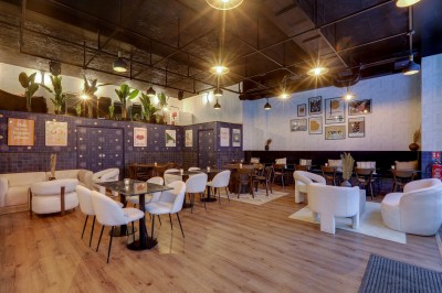 Intérieur d'un bar moderne avec comptoir éclairé, étagères de bouteilles, tables et chaises dans une ambiance chaleureuse.