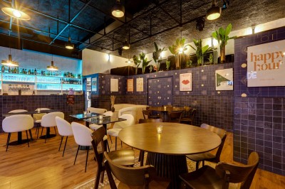 Intérieur d'un bar moderne avec comptoir éclairé, étagères de bouteilles, tables et chaises dans une ambiance chaleureuse.