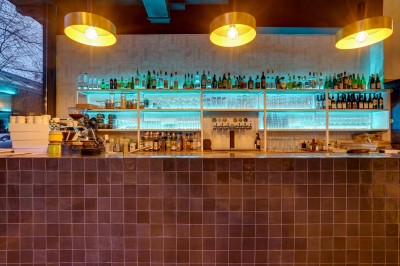 Intérieur d'un bar moderne avec comptoir éclairé, étagères de bouteilles, tables et chaises dans une ambiance chaleureuse.