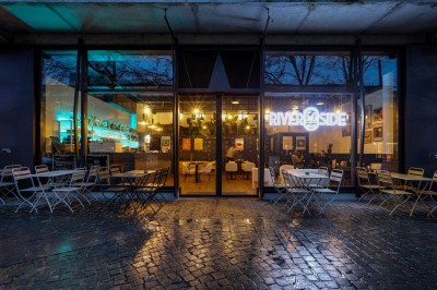 Intérieur d'un bar moderne avec comptoir éclairé, étagères de bouteilles, tables et chaises dans une ambiance chaleureuse.