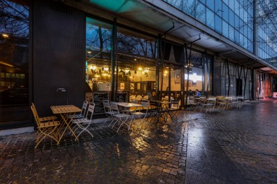 Intérieur d'un bar moderne avec comptoir éclairé, étagères de bouteilles, tables et chaises dans une ambiance chaleureuse.