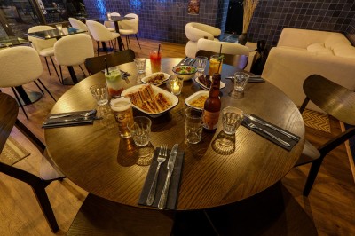 Intérieur d'un bar moderne avec comptoir éclairé, étagères de bouteilles, tables et chaises dans une ambiance chaleureuse.