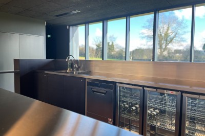 Cuisine professionnelle équipée avec plan de travail inox, fours, hotte, micro-ondes et sol carrelé gris.