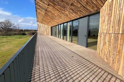 Cuisine professionnelle équipée avec plan de travail inox, fours, hotte, micro-ondes et sol carrelé gris.
