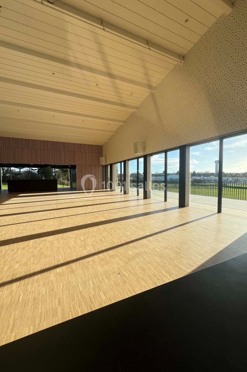 Salle lumineuse avec parquet clair, grandes baies vitrées donnant sur un espace extérieur verdoyant.