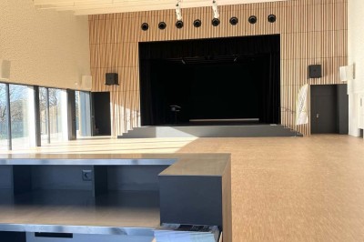 Cuisine professionnelle équipée avec plan de travail inox, fours, hotte, micro-ondes et sol carrelé gris.